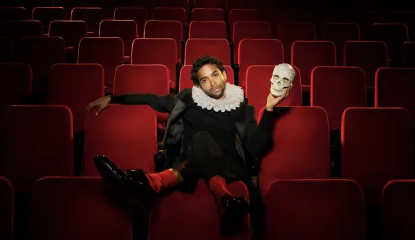 Man in Renaissance-style clothing with large white color sits in red theater chais holding skull